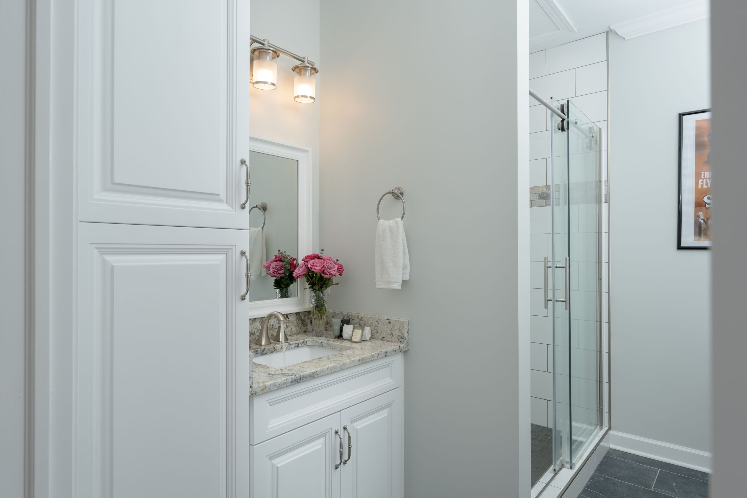 Reagan Bathroomw with granite countertop sink, white storage cabinet and glass door on shower